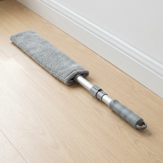 Retractable gap duster laid on a wooden floor beside a baseboard