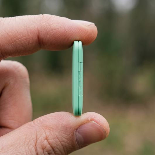 Green item finder tag held between fingers showing thin profile