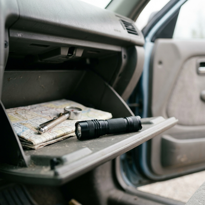 Black pocket flashlight stored in a car glovebox with a map and tire gauge